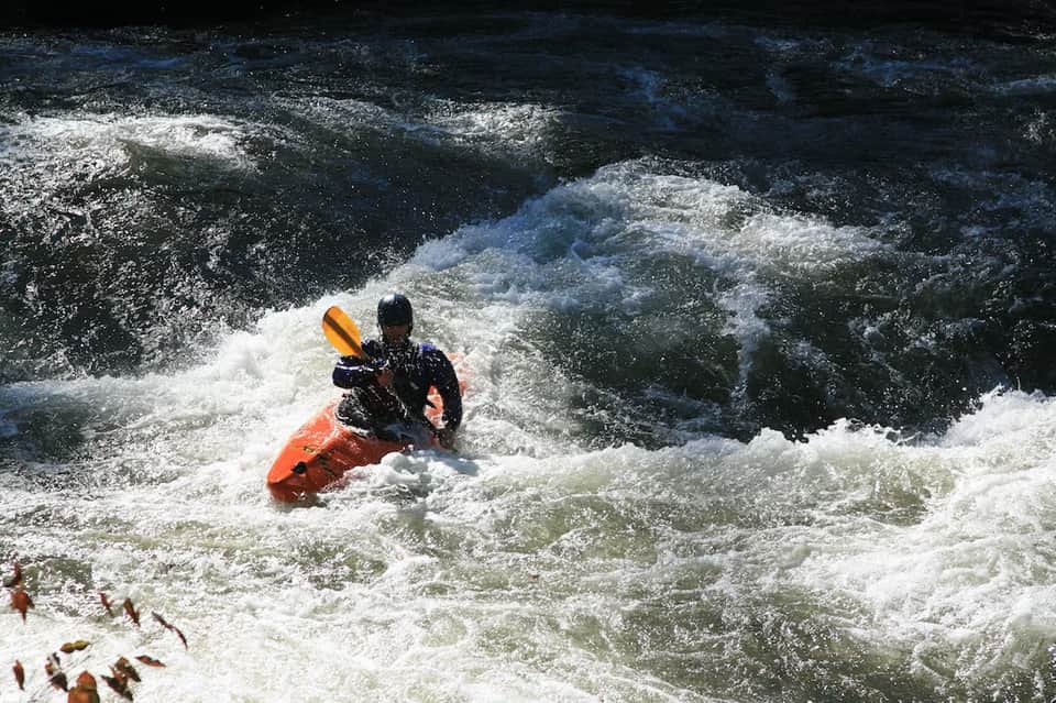 Kayaker in orange and black gear paddling through whitewater ocean waves