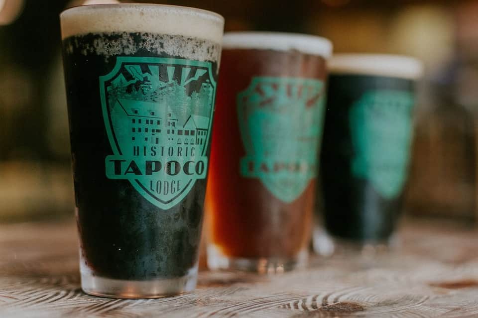 Three glasses of craft beer with Historic Tapoco Lodge branding on wooden surface