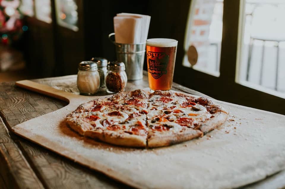 Pizza and beer served on wooden table with salt and pepper shakers