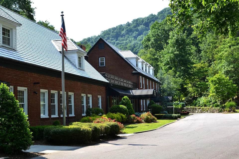 Historic brick lodge building with white trim, American flag, and mountain forest backdrop