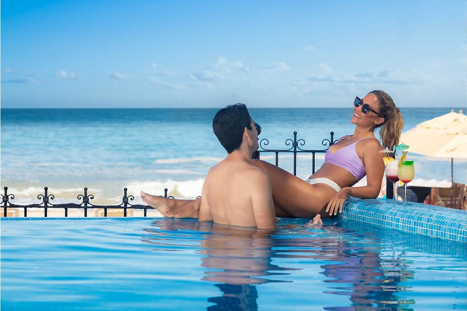 Couple relaxing in oceanfront pool with tropical cocktails and ocean view in background