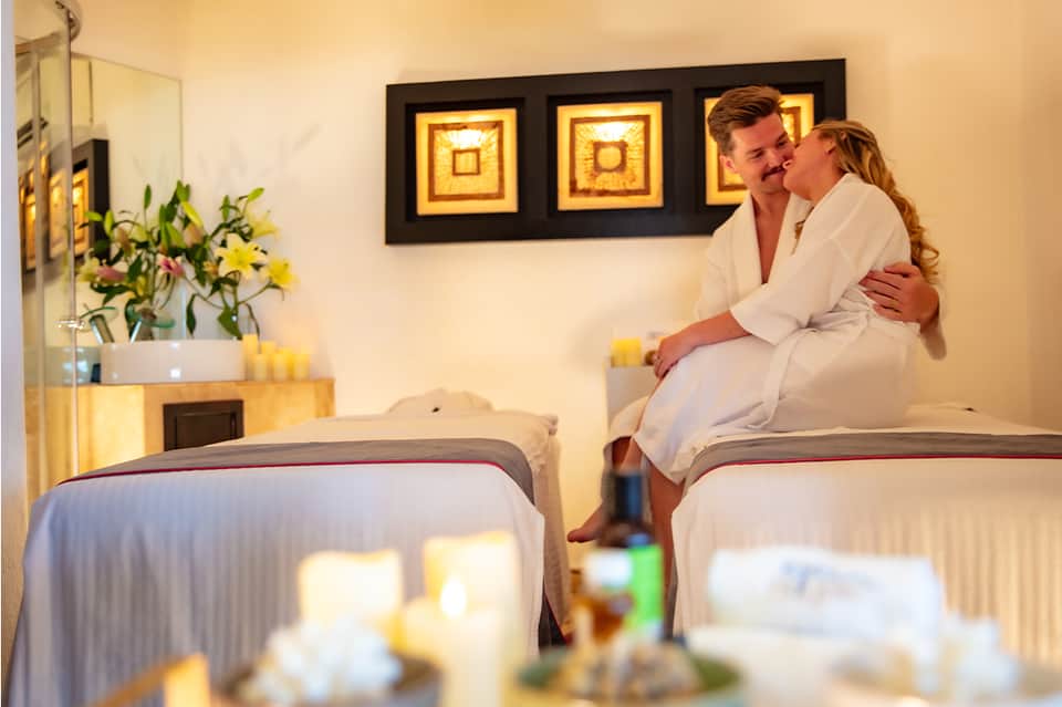 Couple sitting on bed in hotel room with flower arrangement and framed artwork