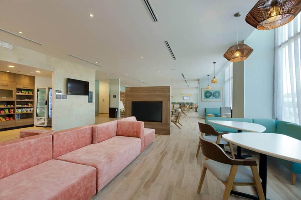 Contemporary hotel lobby with pink sofa, wooden accents, and turquoise seating areas
