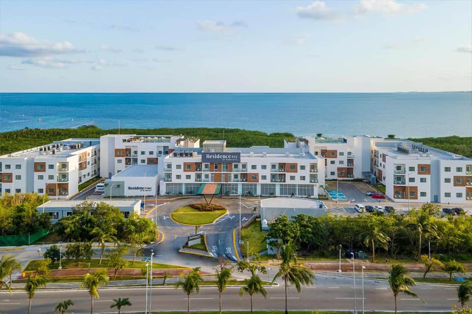 Oceanfront resort complex with white buildings overlooking turquoise water and palm trees