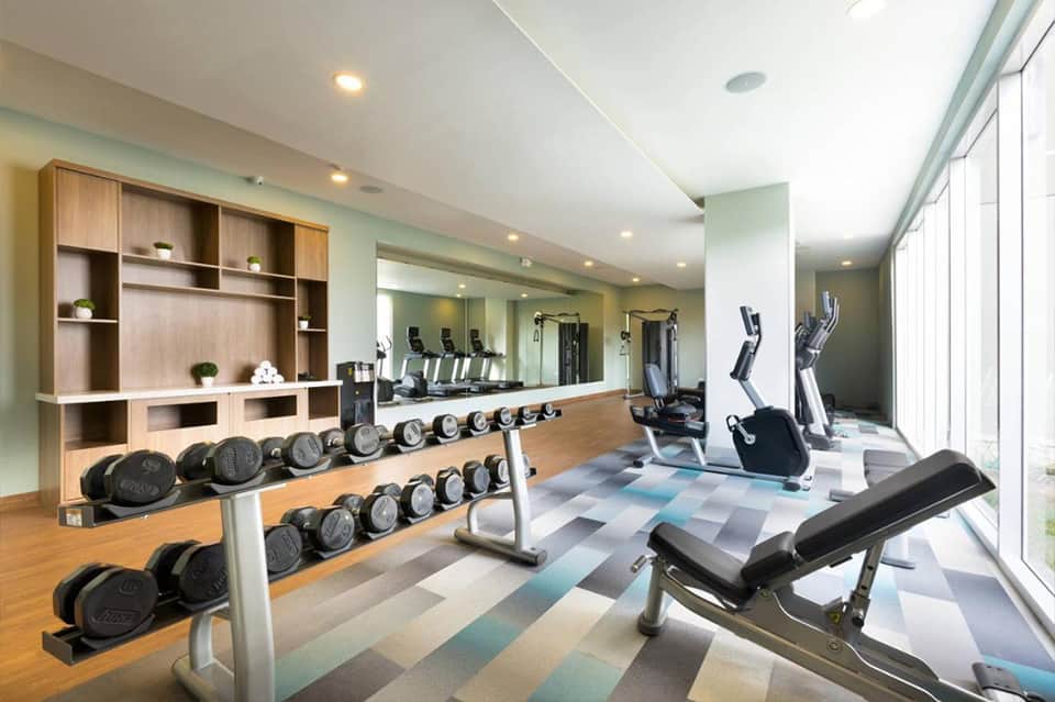Fitness center with dumbbell racks, exercise equipment, mirrors, and large windows with natural light