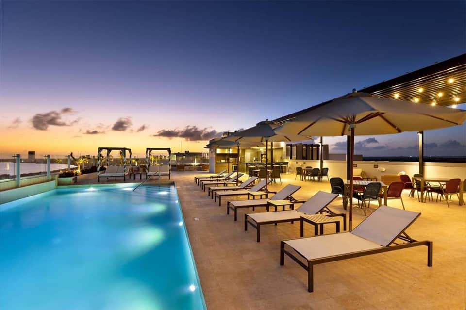 Elegant rooftop pool at dusk with lounge chairs, umbrellas, and city lights