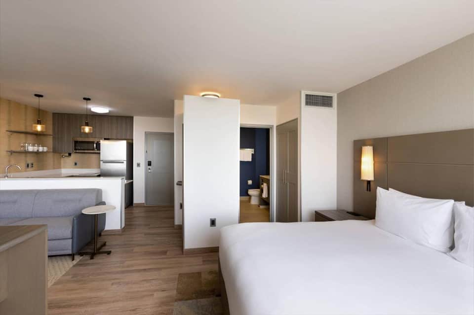 Modern hotel studio with kitchenette, bed, seating area, and open floor plan layout