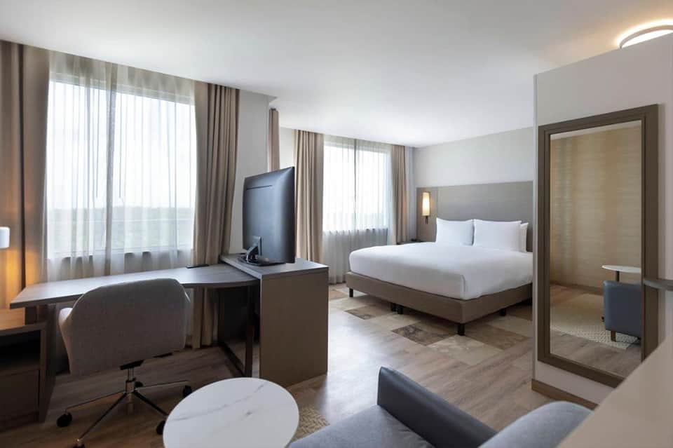 Contemporary hotel suite with bed, work desk, TV, and floor-to-ceiling windows
