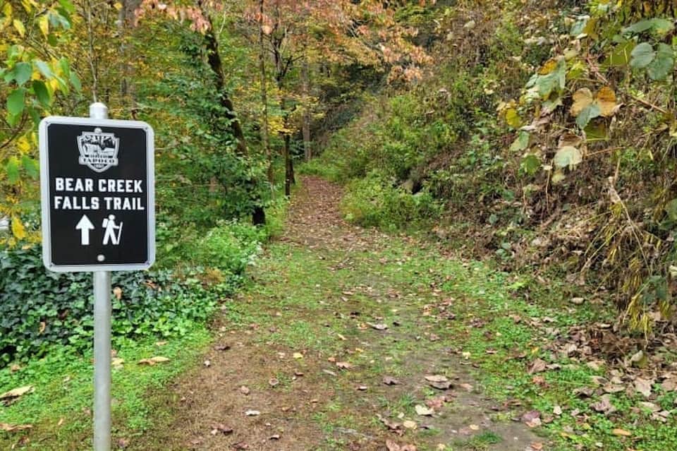 Bear Creek Falls Trail sign marking hiking path through lush green forest with autumn foliage