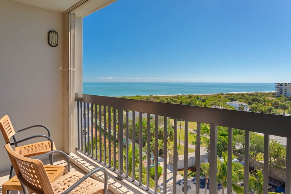 Oceanfront balcony with ocean view, vegetation, and wooden railing from upper floor room
