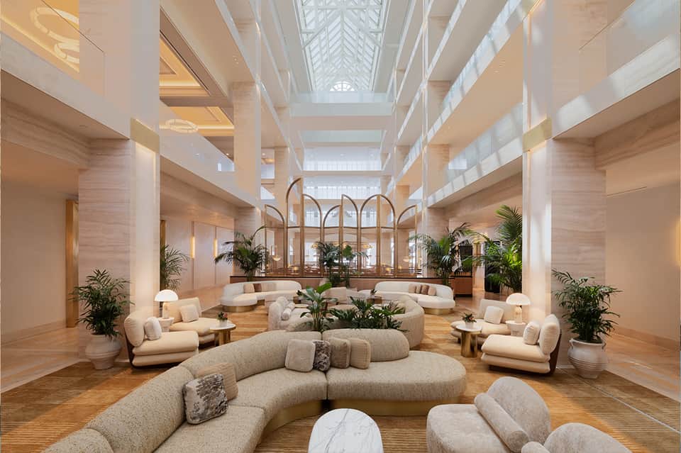 Modern hotel lobby with curved cream seating, skylights, potted plants, and minimalist design