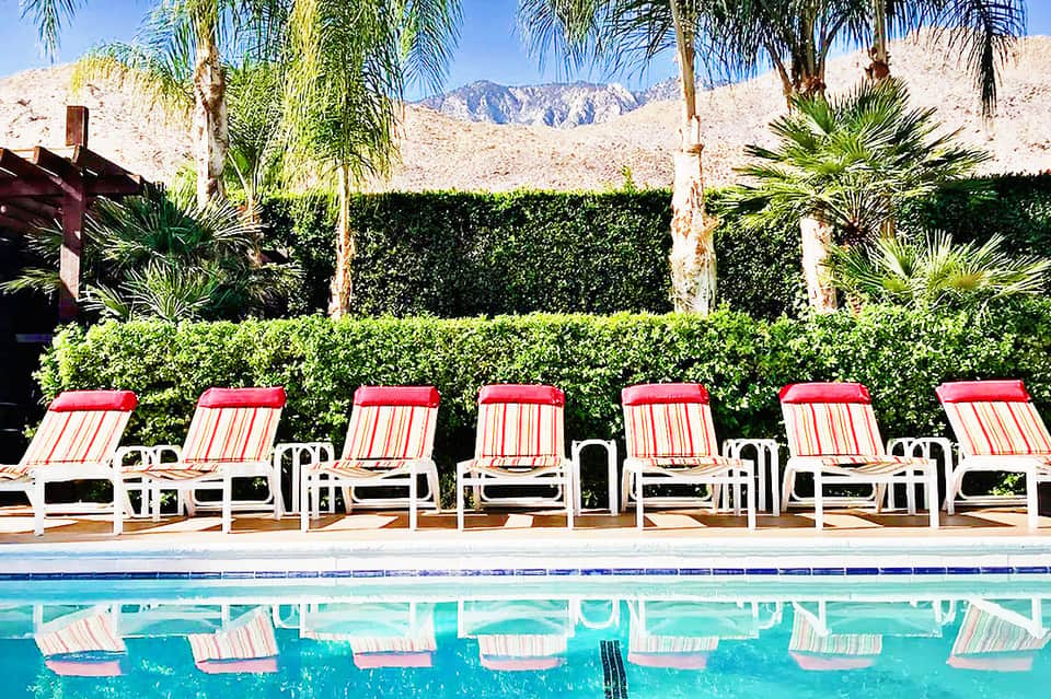 Red and white striped lounge chairs lined up by pool with palm trees and desert mountains