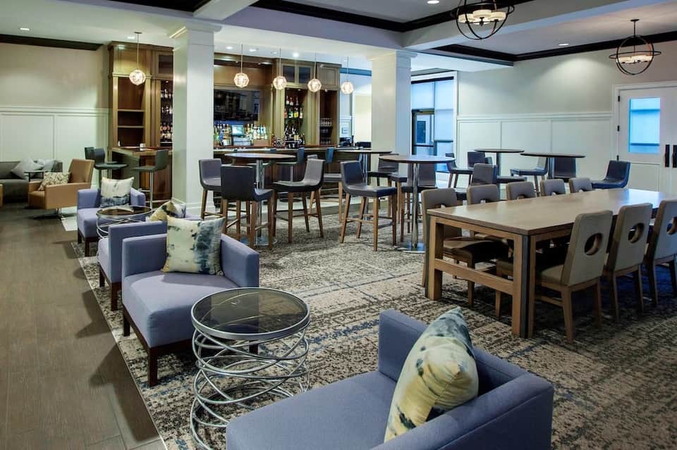 Upscale lounge with blue seating, bar area, wooden cabinetry, pendant lighting, and dining tables