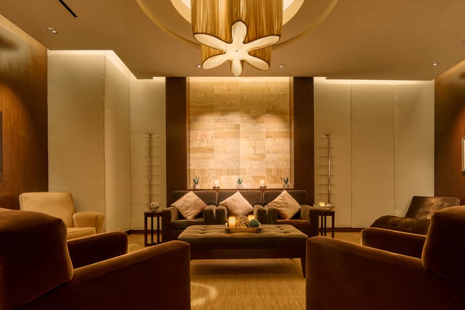 Warm-toned spa relaxation room with bronze leather seating and illuminated stone accent wall