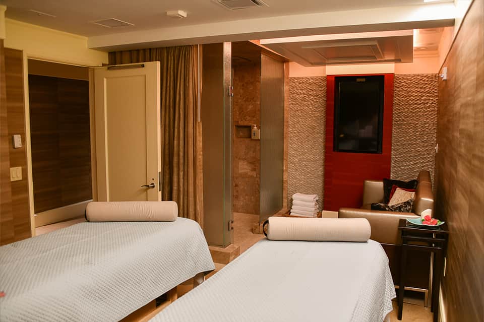 Dual massage bed spa room with brown tones and warm lighting
