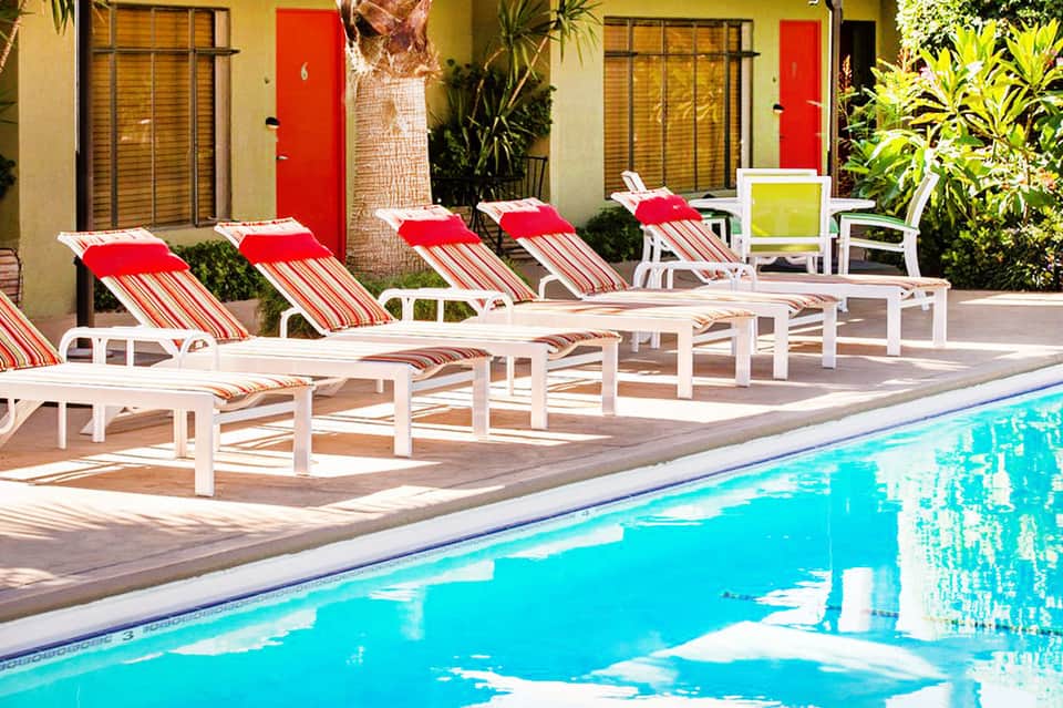 Resort pool with red and white striped lounge chairs, bright turquoise water, yellow building backdrop