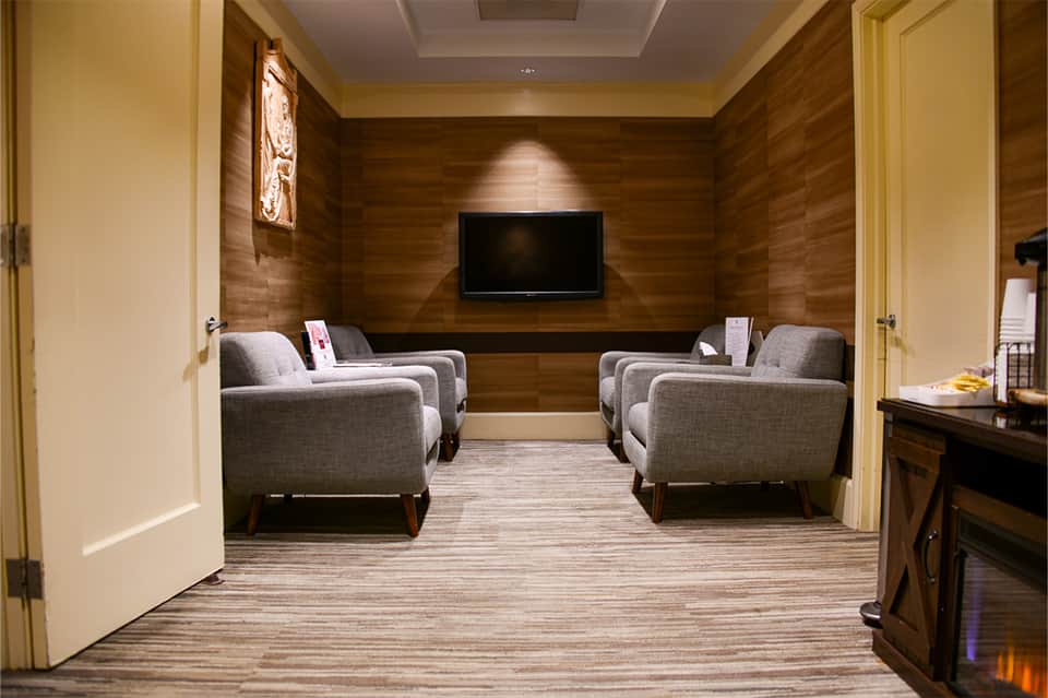 Private home theater with four gray upholstered armchairs facing a wall-mounted TV, warm wood paneling
