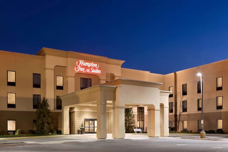 Hampton Inn & Suites exterior at night with tan stucco walls, columns, and illuminated neon sign