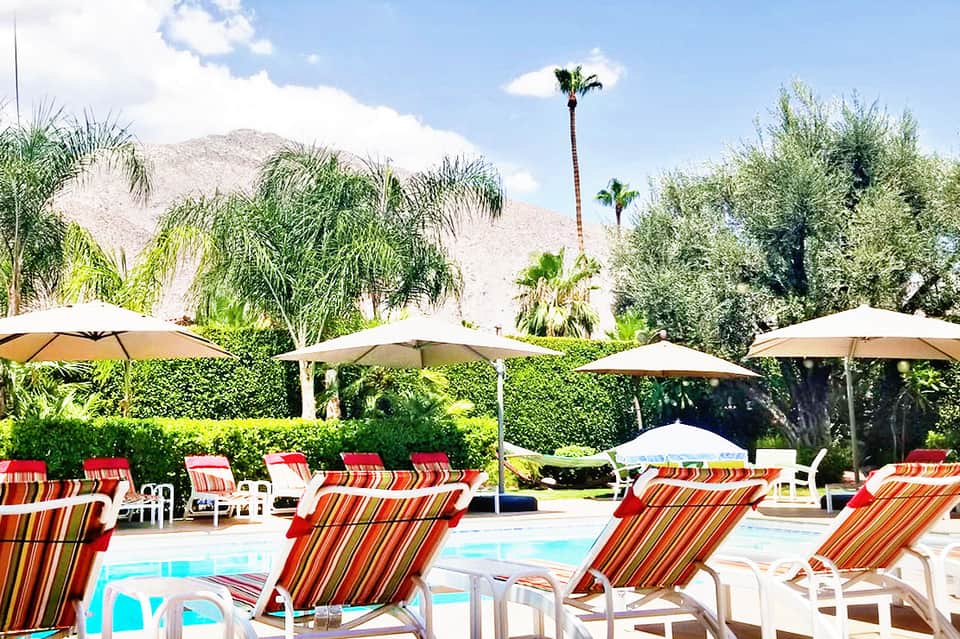 Resort pool area with striped lounge chairs, umbrellas, and mountain backdrop in desert landscape