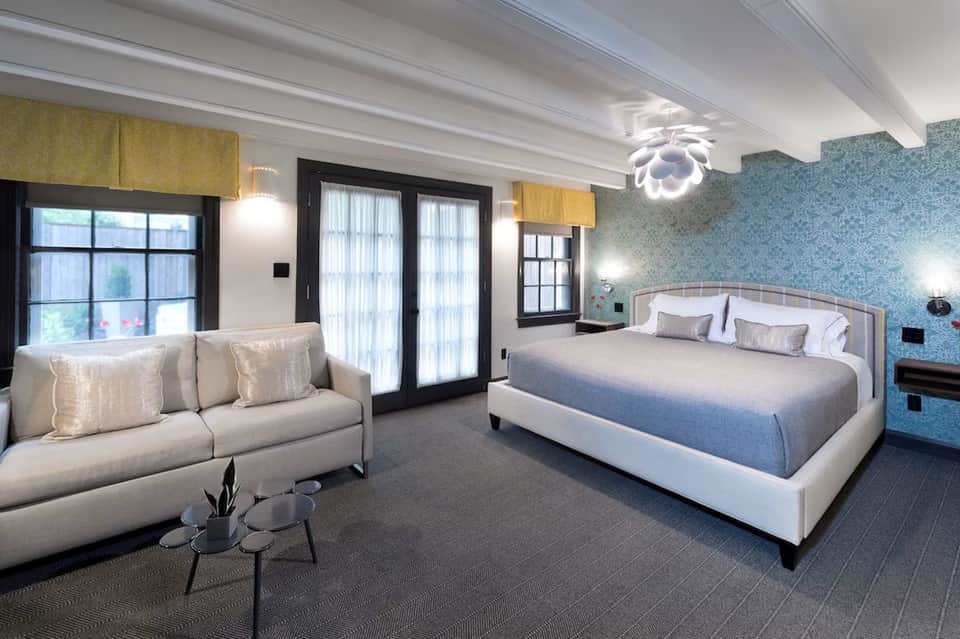 Luxury hotel suite with king bed, sitting area, blue patterned wallpaper, and modern lighting