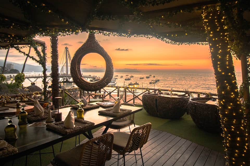 Beachfront dining terrace at sunset with decorative circular sculpture framing the ocean view