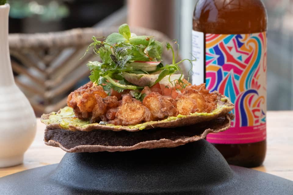 Gourmet fried shrimp sandwich with fresh greens and colorful craft beer bottle on dark plate