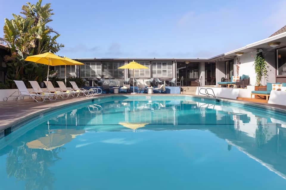 Luxury pool area with turquoise water, yellow umbrellas, lounge chairs, white building, and palm landscaping