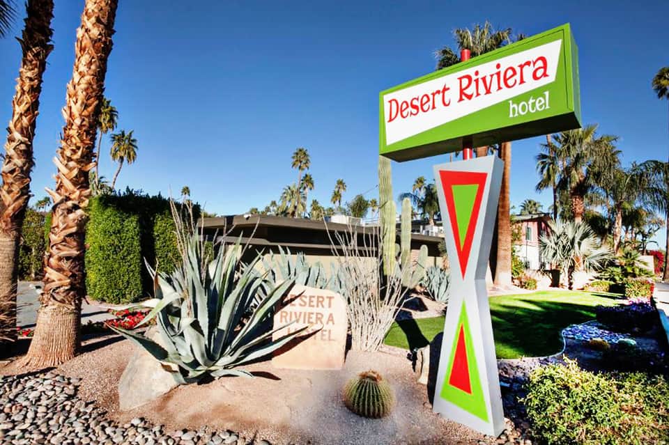 Desert Riviera Hotel sign with palm trees and desert landscaping