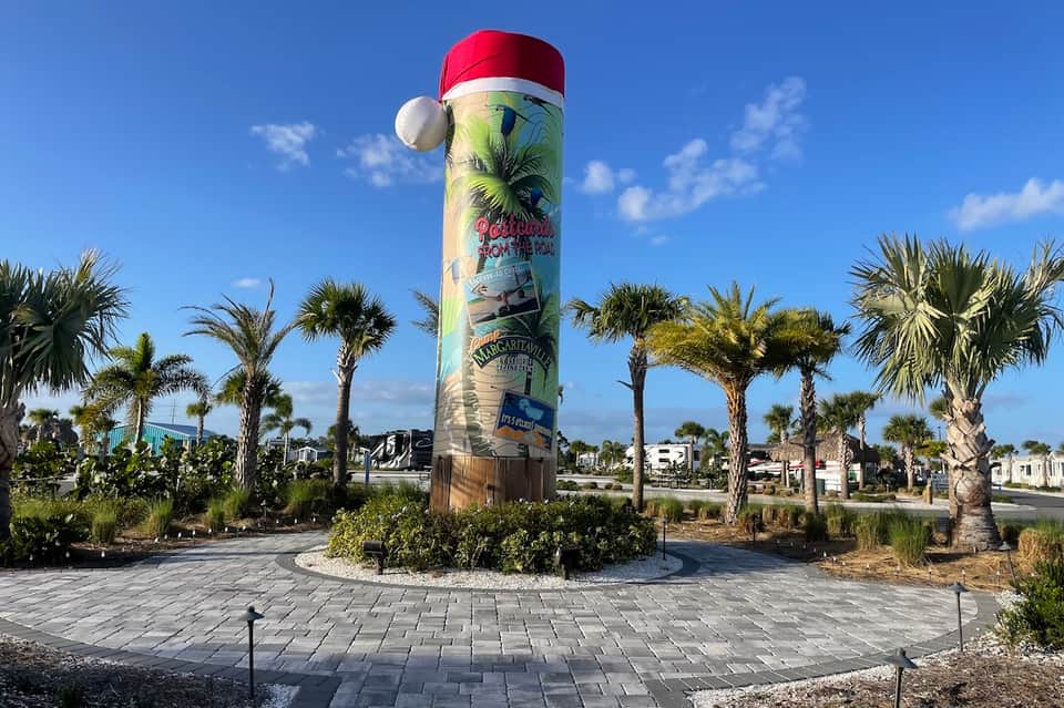 Decorated cylindrical monument with Santa hat and palm trees in landscaped roundabout during holidays