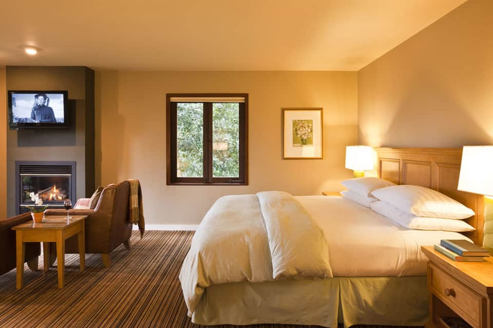 Luxurious hotel bedroom with fireplace, warm lighting, wooden headboard, and comfortable furnishings