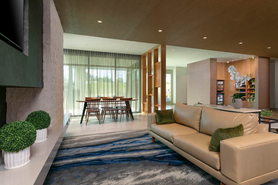 Modern hotel lobby with beige sofa, dining area, wooden accents, and contemporary design