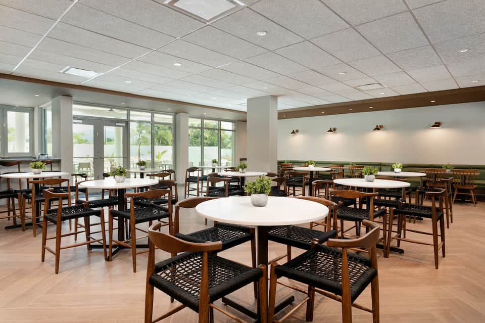 Contemporary dining hall with round white tables, wooden chairs, and wall-to-wall windows