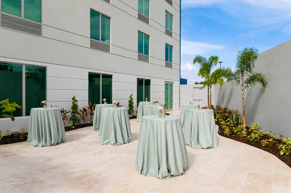Modern courtyard with pale green tablecloths on round tables, white building facade, and palm trees