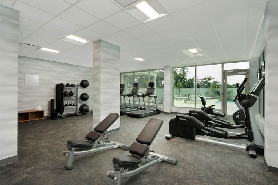Modern fitness center with exercise bikes, weight benches, and large windows overlooking outdoor area