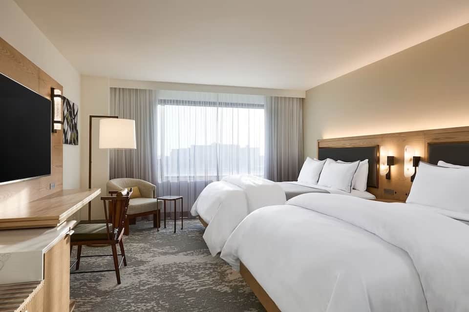 Modern hotel bedroom with two double beds, desk, and balcony with ocean views