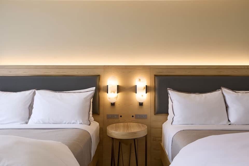 Twin queen beds in hotel room with wooden headboard, accent lighting, and side table