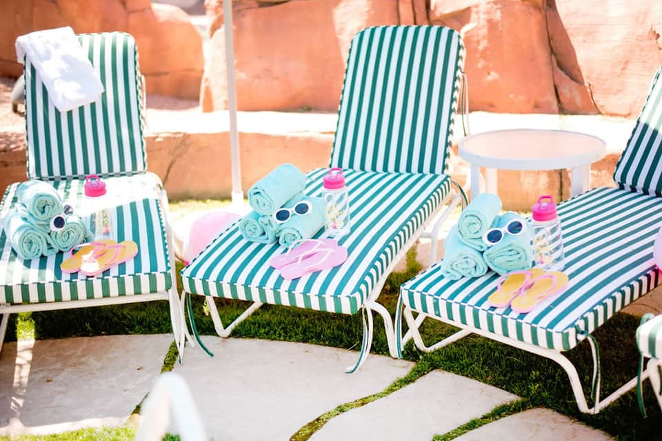 Green and white striped lounge chairs with colorful beach accessories arranged poolside