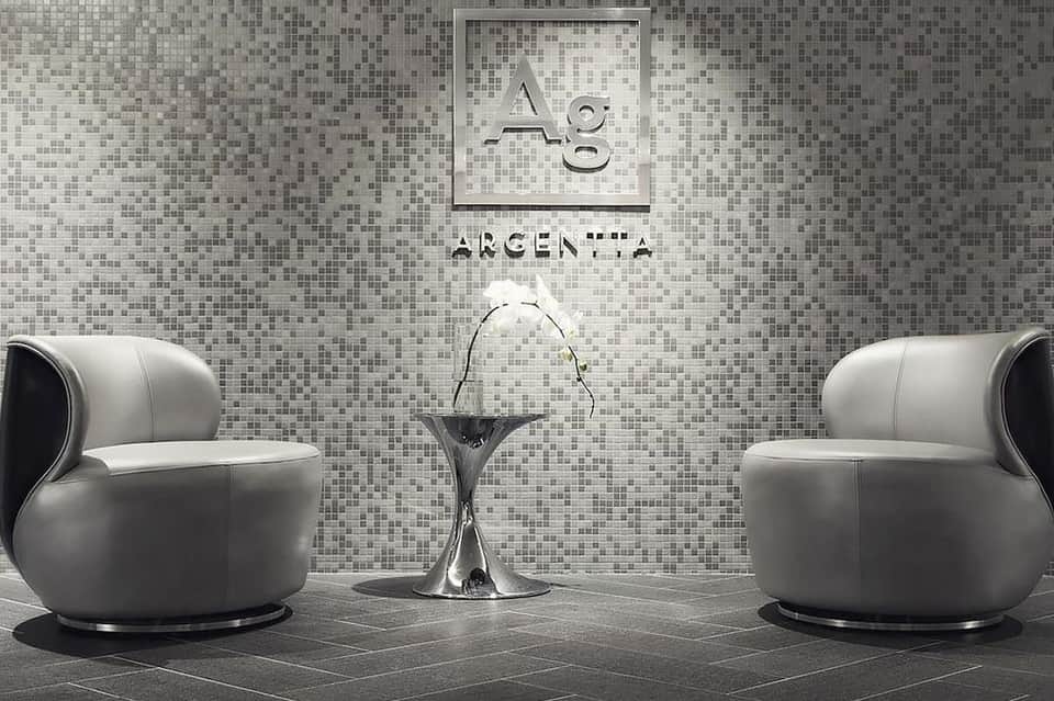 Minimalist spa lounge with mosaic tile walls, two modern white armchairs, and small round table