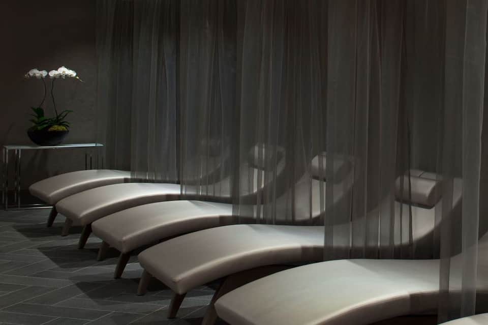 Spa relaxation area with curved white lounge seating and sheer gray curtains creating dramatic shadow patterns