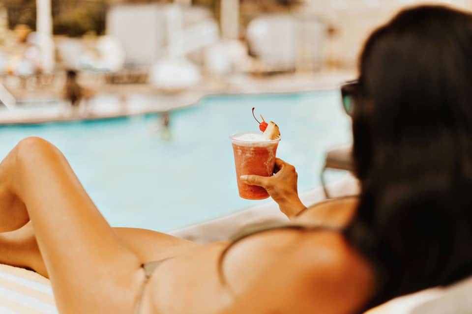 Woman relaxing by pool holding tropical cocktail with cherry garnish
