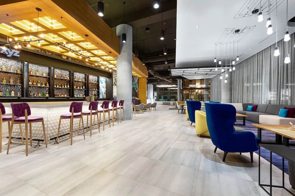 Contemporary hotel lobby and bar area with purple chairs, wooden ceiling, and modern lounge seating