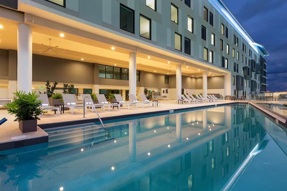 Indoor pool with blue water, lounge chairs, and modern hotel building at dusk
