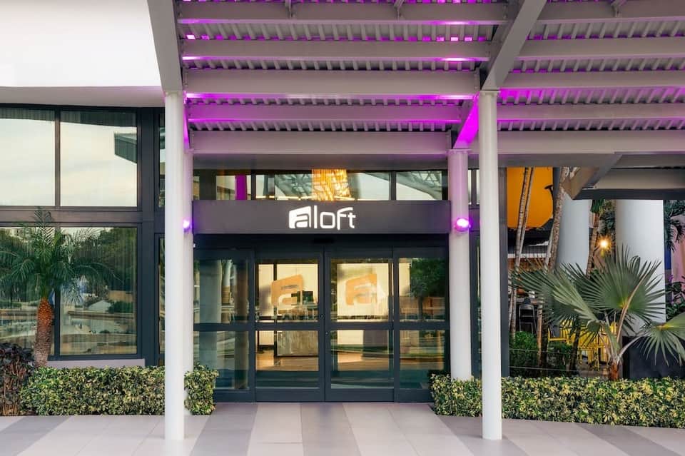 Aloft hotel entrance at night with purple neon lighting, white columns, and glass doors