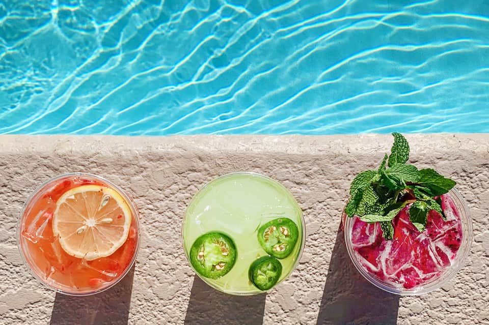 Three colorful tropical cocktails with citrus and herbs on poolside concrete deck