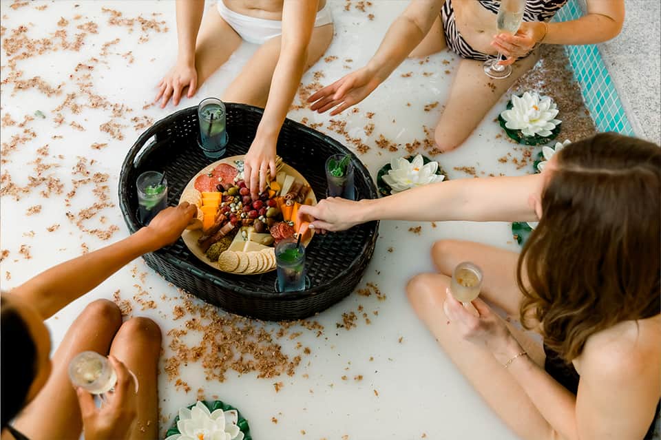 Overhead view of friends sharing a charcuterie platter on a white surface with water lily decorations