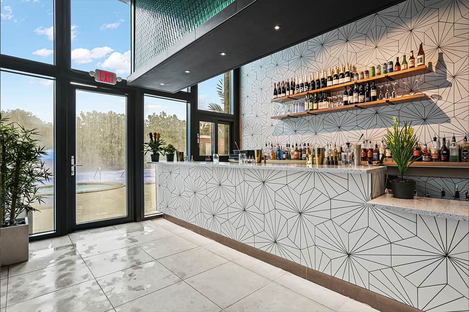 Modern bar interior with geometric tile wall, wooden shelves with liquor bottles, and large windows