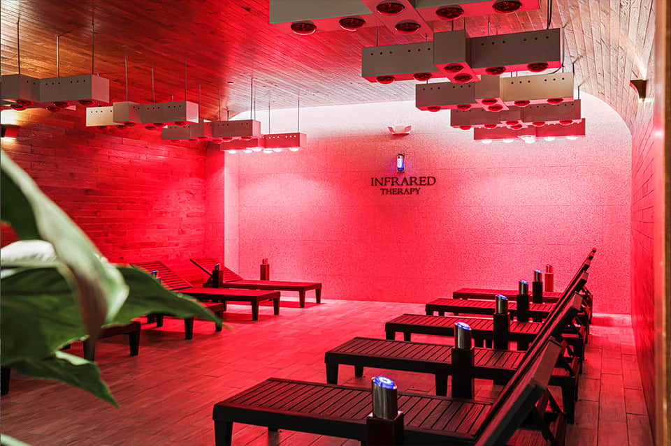 Infrared therapy room with red lighting, wooden benches, and hanging heating elements for wellness treatments