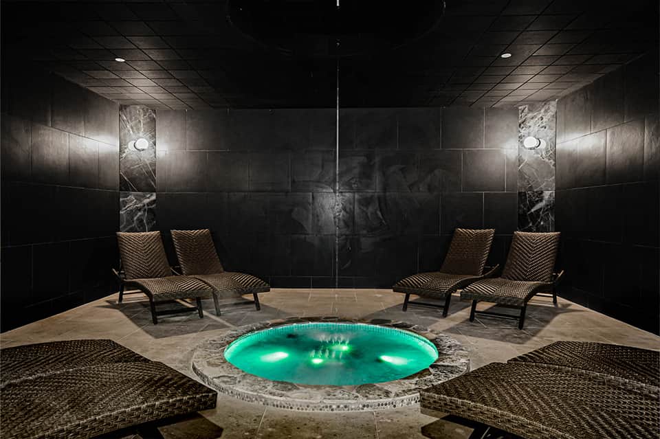 Luxurious spa area with glowing turquoise hot tub, marble walls, and woven lounge chairs