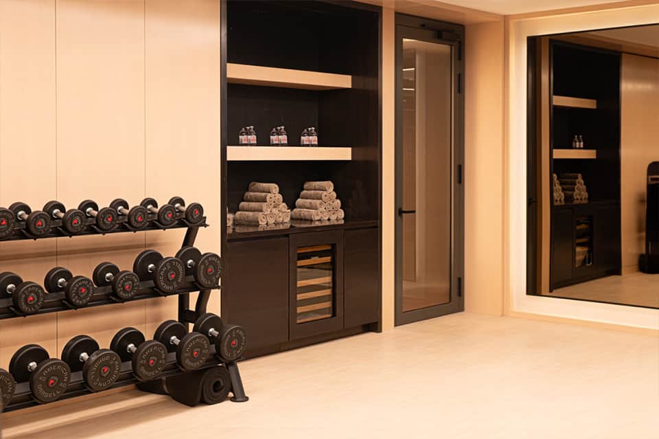 Modern fitness center with dumbbell racks, black shelving units displaying towels, and mirrored walls