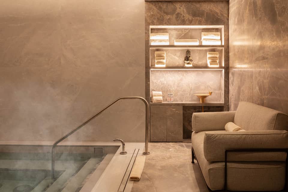 Spa relaxation room with soaking tub and illuminated wall shelving